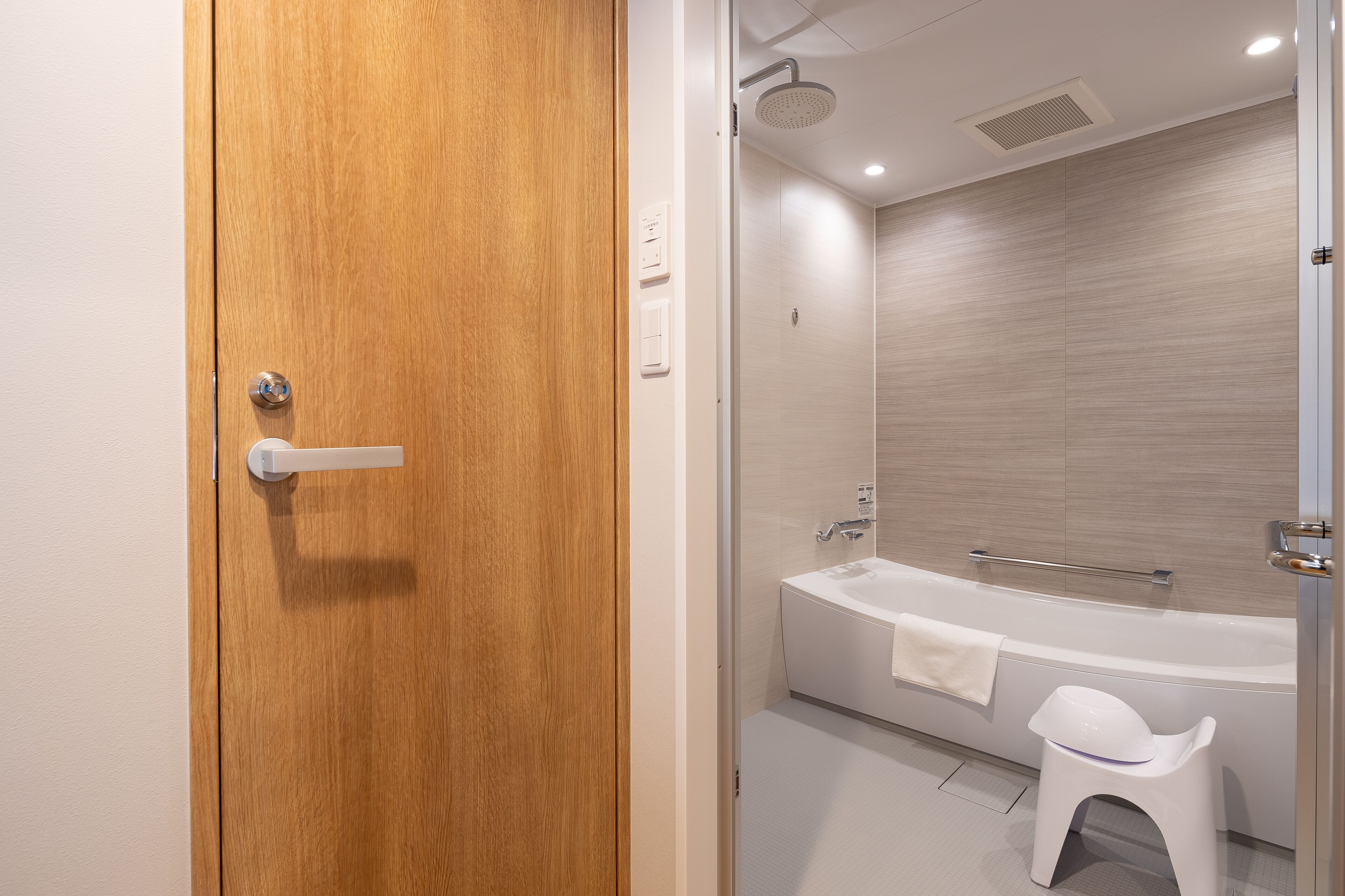 A modern bathroom with a wooden door, a white bathtub, and a small white stool.