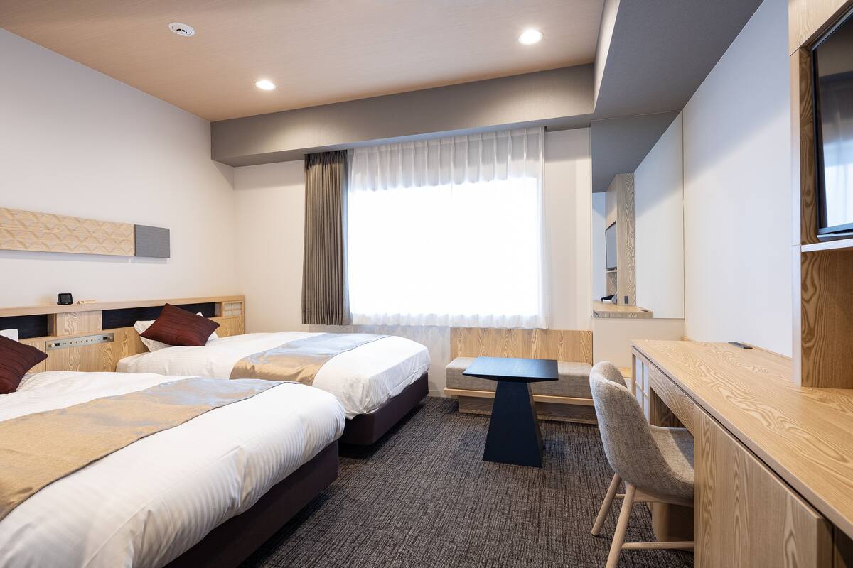Een hotelkamer met twee bedden, een bureau en een stoel.