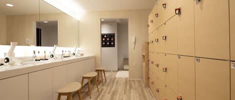 Un baño moderno con un lavamanos alargado, taburetes de madera y una fila de taquillas.