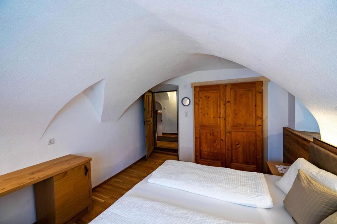 A bedroom with a sloped ceiling, wooden wardrobe, and a bed with a white mattress.
