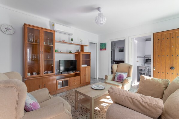 A living room with a TV, wooden cabinets, a sofa, a chair, and a table.