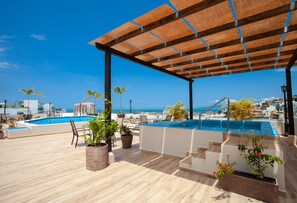 Ein Poolbereich auf dem Dach mit einer Holzpergola, Liegestühlen und Topfpflanzen.