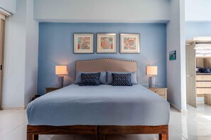Ein Schlafzimmer mit einem Bett, zwei Nachttischlampen und drei gerahmten Kunstwerken an der Wand.