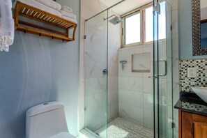 Ein modernes Badezimmer mit einer gläsernen Duschkabine, einer Toilette und einem hölzernen Handtuchhalter.