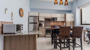 A modern kitchen with a central island, stainless steel appliances, and a dining area with wicker chairs. - 5 min to Los Muertos Beach in front of Cuale River located in Isla Cuale! 1BD Co (Puerto Vallarta)