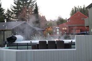 Ein Sauna-Bereich mit einem großen Wassertank, einer überdachten Sitzgelegenheit mit Stühlen und Blick auf Wohnhäuser im Hintergrund.