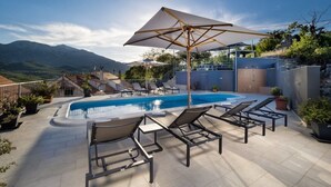 Un espace piscine aménagé sur le toit, avec des chaises longues et des parasols, entouré de montagnes et surplombant un ciel dégagé.