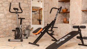 Une salle de sport à domicile équipée de matériel d’exercice, notamment un vélo d’appartement, un banc de musculation et un appareil de rameur.