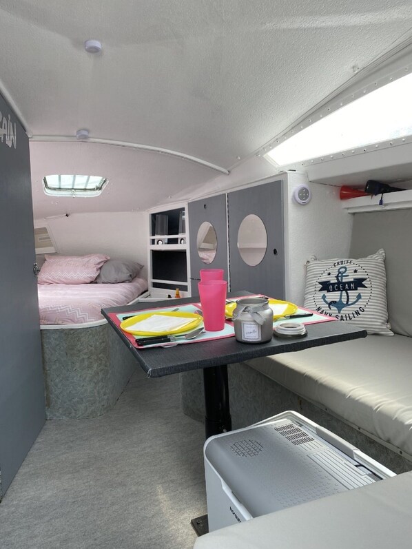A compact RV interior with a bunk bed, a small kitchenette, a table with a jar, and a pillow with nautical theme.