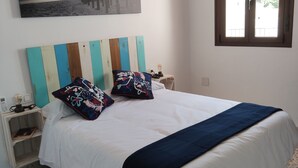 Una camera da letto con un letto, un comodino, una lampada, una finestra e un quadro appeso al muro.