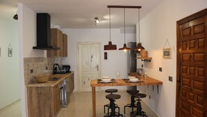 Una cucina con pensili in legno, un'isola centrale con sgabelli, lampade a sospensione e una porta con motivo geometrico.