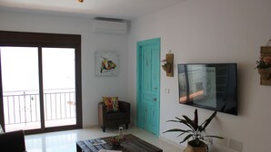 Un soggiorno con un divano, un tavolino da caffè, una porta color turchese, una TV montata a parete e un balcone con ringhiera.
