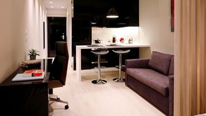 A modern living room with a sofa, a desk with a laptop, and two bar stools. - Segundo Molo Suites (Thessaloniki)