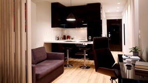 A modern living room with a sofa, a dining area with a table and chairs, and a kitchen in the background. - Segundo Molo Suites (Thessaloniki)