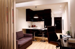 A modern living room with a sofa, a dining area with a table and chairs, and a kitchen in the background.