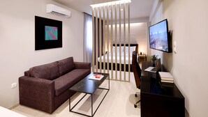 A modern hotel room with a sofa, a coffee table, a desk with a laptop, a TV, and a bed. - Segundo Molo Suites (Thessaloniki)