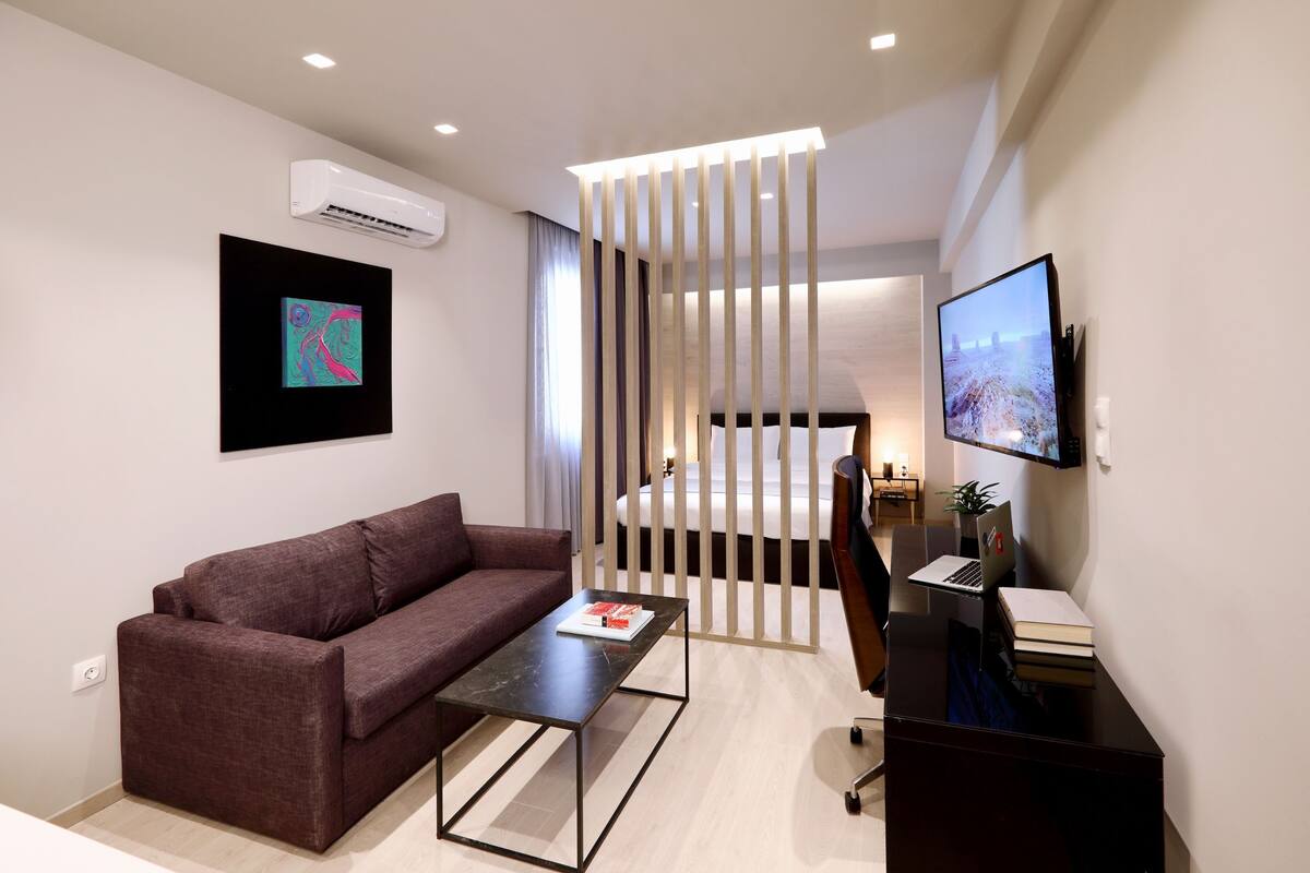 Une chambre d’hôtel moderne équipée d’un canapé, d’une table basse, d’un bureau avec un ordinateur portable, d’une télévision et d’un lit.