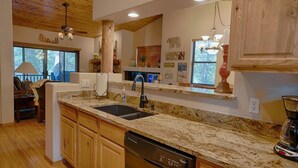 A kitchen with granite countertops, a dishwasher, wooden cabinets, a double sink, and a ceiling fan.