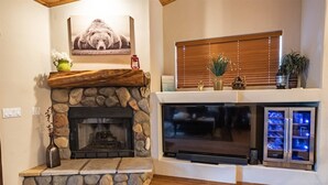 A stone fireplace with a TV, a wooden mantel, and a window with blinds.