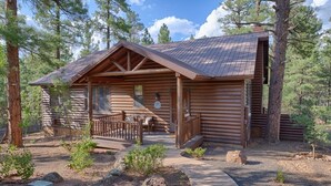 A log cabin with a porch, a small deck, and a pathway leading to the entrance.