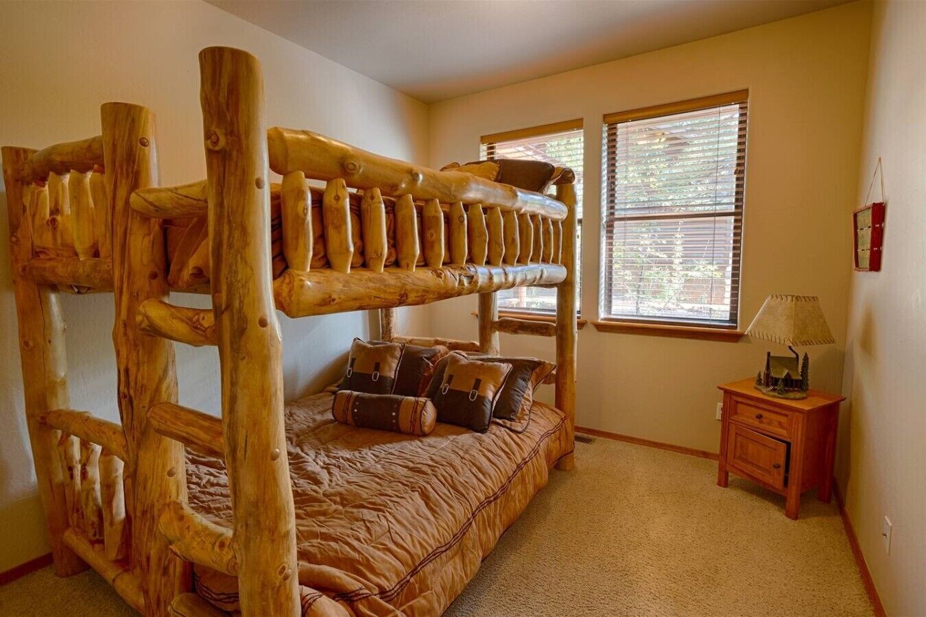 A bunk bed with a wooden frame, a small bedside table with a lamp, and a window with blinds.