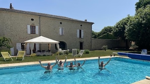 A swimming pool with four people in the water, a covered patio area, and a stone building in the background. - Mas DISTAISE, 5 bedrooms, 4 bathrooms, pool, billiards.  Vacations with family and friends (Grane)