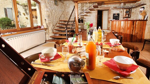 A rustic dining area with a wooden table set for a meal, a stone wall, and a staircase leading to an upper level. - Mas DISTAISE, 5 bedrooms, 4 bathrooms, pool, billiards.  Vacations with family and friends (Grane)