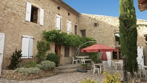 A stone building with white shutters, a patio with white chairs and a red umbrella, and greenery around. - Mas DISTAISE, 5 bedrooms, 4 bathrooms, pool, billiards.  Vacations with family and friends (Grane)