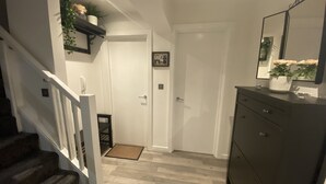 Un couloir avec un escalier, une porte, une commode de couleur sombre et un miroir.