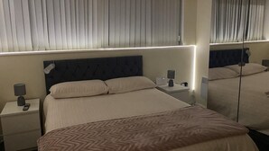 Une chambre d’hôtel avec un grand lit, des tables de chevet, une petite table, une lampe et un miroir.