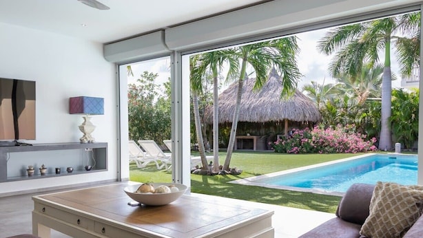 A modern living room with a large window, a pool, and a thatched-roof structure.