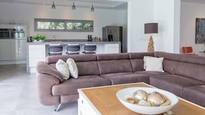 A modern living room with a large sectional sofa, a coffee table, and a kitchen in the background.