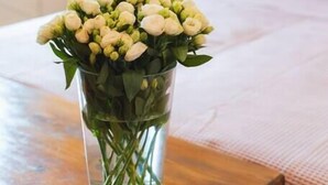 A clear glass vase with flowers on a wooden table in a room.