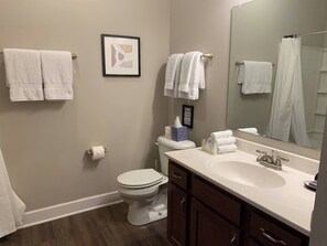 Ein Badezimmer mit Toilette, Waschbecken und Spiegel. Handtücher hängen an der Wand, und ein gerahmtes Bild befindet sich über der Toilette.