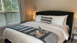 Una cama bien tendida con un almohadón a rayas, una lámpara de noche y una bandeja con botellas y una vela.