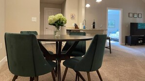Un comedor con una mesa redonda y cuatro sillas, un jarrón con flores, y una cocina al fondo.