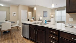 A modern kitchen with dark wood cabinets, a white countertop, and a dishwasher. There is a dining area with a round table and chairs. - Dublin 2BR | Pet friendly | 0 stairs | King bed (Dublin)