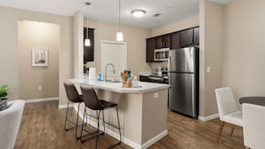 A modern kitchen with a central island, dark cabinets, stainless steel appliances, and a dining area with two chairs. - Dublin 2BR | Pet friendly | 0 stairs | King bed (Dublin)