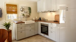 Una cucina moderna con mobili bianchi, un piano di lavoro in legno, forno integrato e una finestra con persiane.