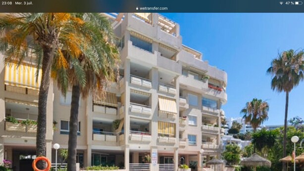 Ein mehrstöckiges Hotel mit Balkonen, einem Schwimmbad und Palmen.