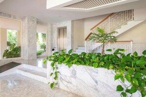 Un vestíbulo amplio con suelo de mármol, una escalera con barandilla de madera y exuberantes plantas verdes.