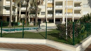 Ein mehrstöckiges Wohngebäude mit Balkonen, einem Schwimmbad und einem eingezäunten Garten.