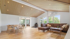 Un salon moderne avec un plafond en bois, un canapé, une table basse et un coin repas comprenant des chaises et une table.