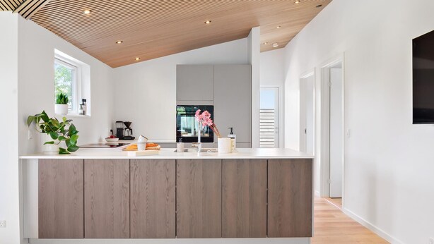 Une cuisine moderne avec un plafond en bois, un grand îlot central et une vue sur l’espace de vie.