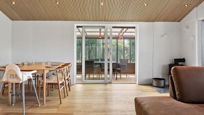 Une pièce spacieuse avec un plafond en bois, un coin repas comprenant une table et des chaises, et une porte-fenêtre coulissante donnant sur un espace extérieur.