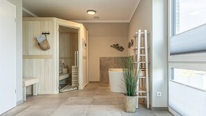 A modern bathroom with a bathtub, a shower, and a wooden vanity. There is a plant in a woven basket and a ladder leaning against the wall. - Stunning home in Büsum with sauna (Büsum)