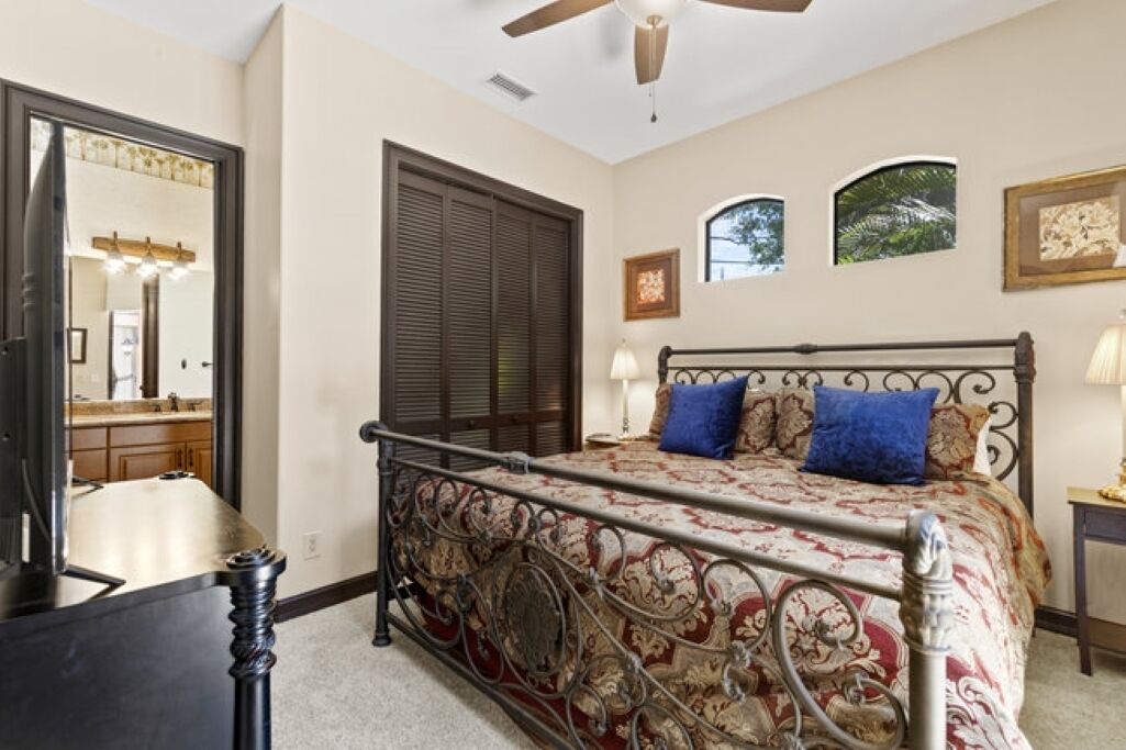 A bedroom with a bed, a nightstand, a lamp, a ceiling fan, a window, and a door.