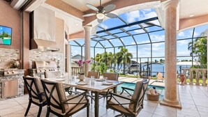 Un vaste espace extérieur aménagé pour les repas, avec vue sur l’océan, une piscine et une cuisine moderne équipée d’un barbecue.