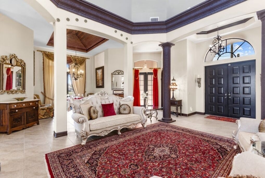 Amplio salón con un gran tapete rojo estampado, un sofá blanco con cojines rojos y una puerta de madera oscura.