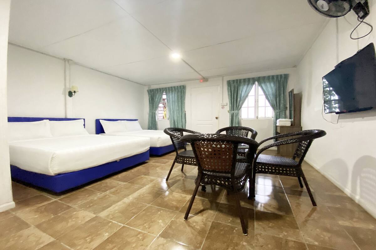 A hotel room with a bed, a dining table with chairs, a TV mounted on the wall, and a window with curtains.
